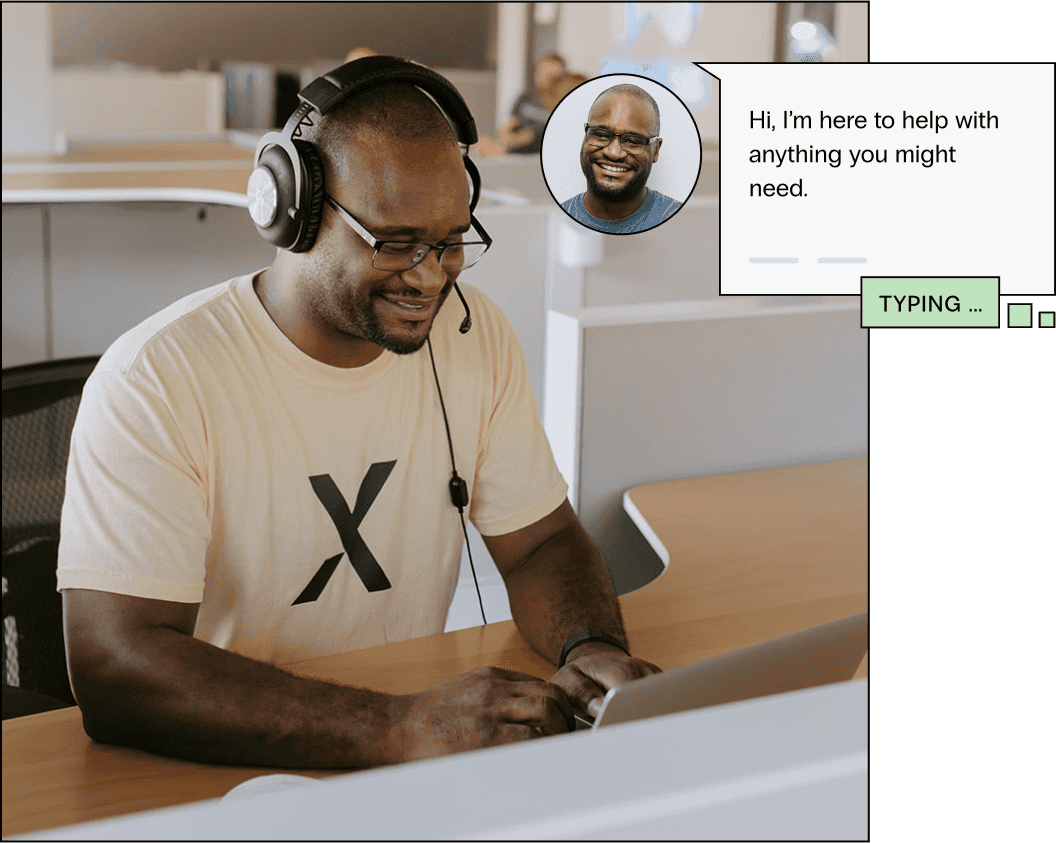 A hosting support representative smiles as he assists a customer at his desk, he types on his computer